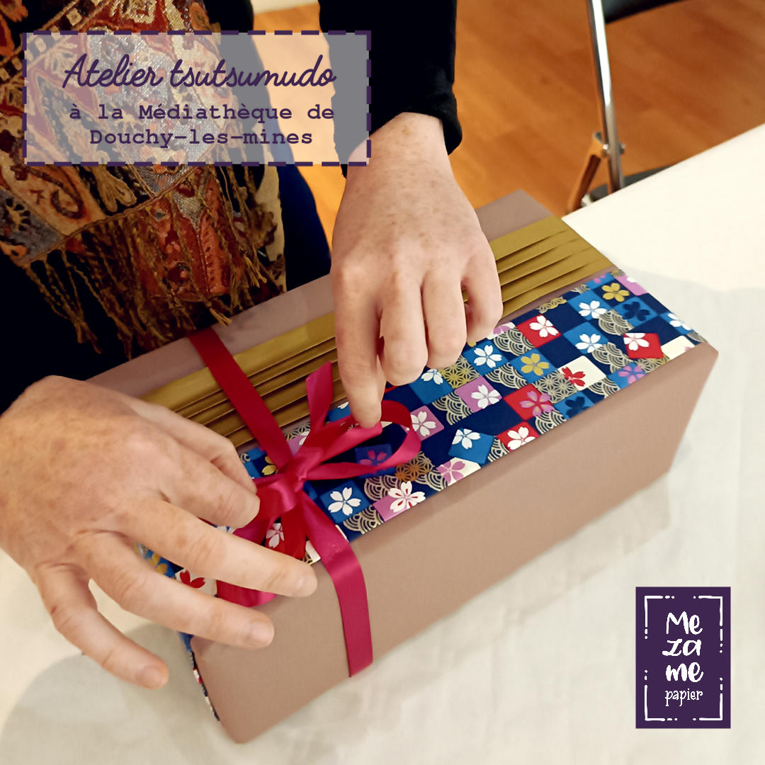 Participante d'un atelier Tsutsumudō nouant un ruban fuchsia sur un paquet cadeau original avec plis décoratifs à la japonaise