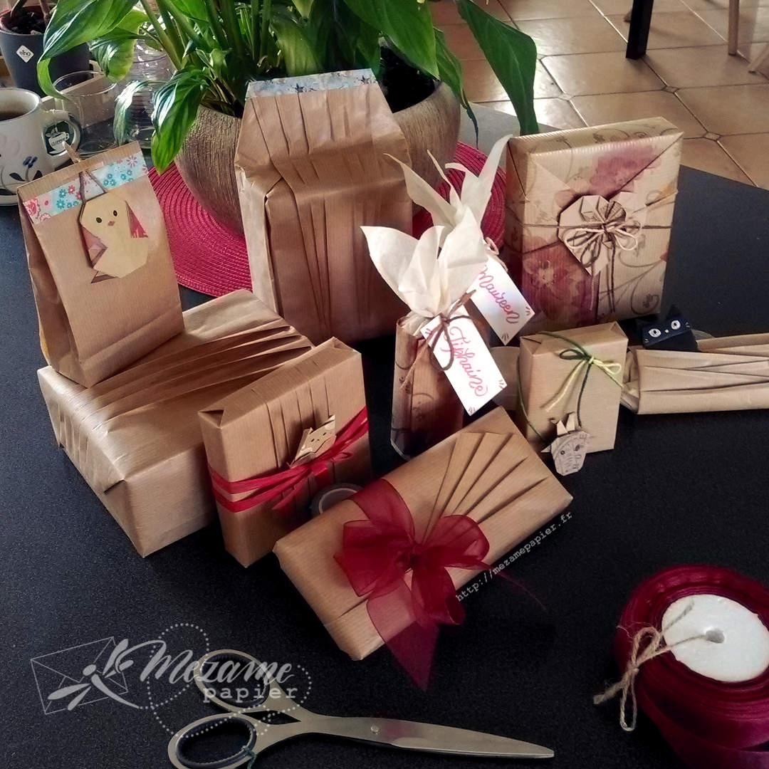 Pile de cadeaux emballés de papier kraft blond avec des plis élégants et des rubans d'organza rouge bordeaux posés sur une table gris foncé